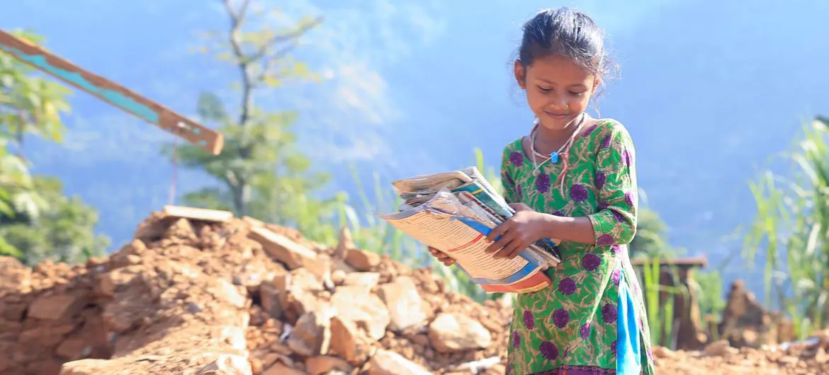 An eight-year-old girl retrieves her textbooks from the rubble of her home, destroyed in an earthquake in western Nepal.