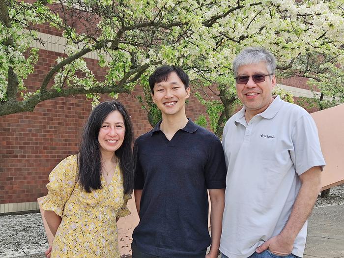 Three individuals standing outside in front of a building and a blooming tree