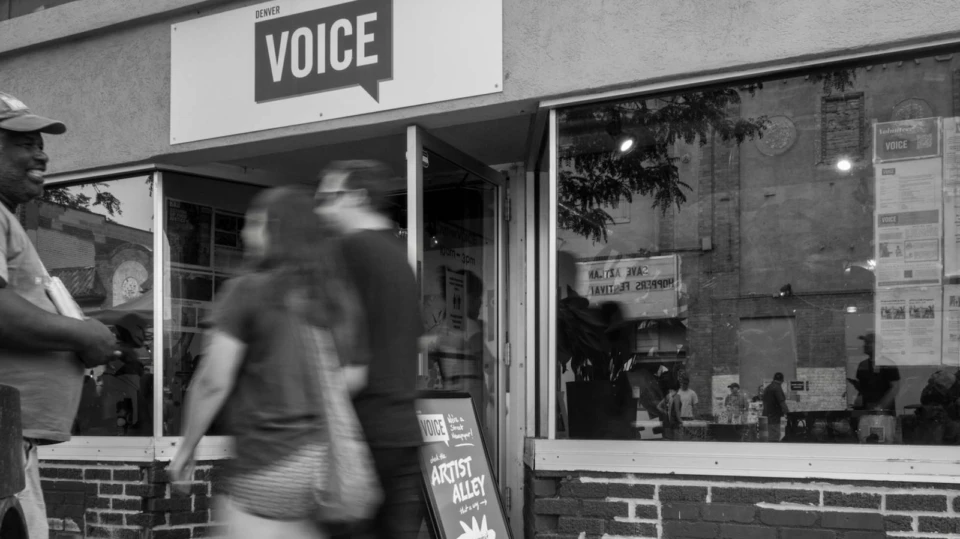 A black and white image of a store front with people walking in front of it