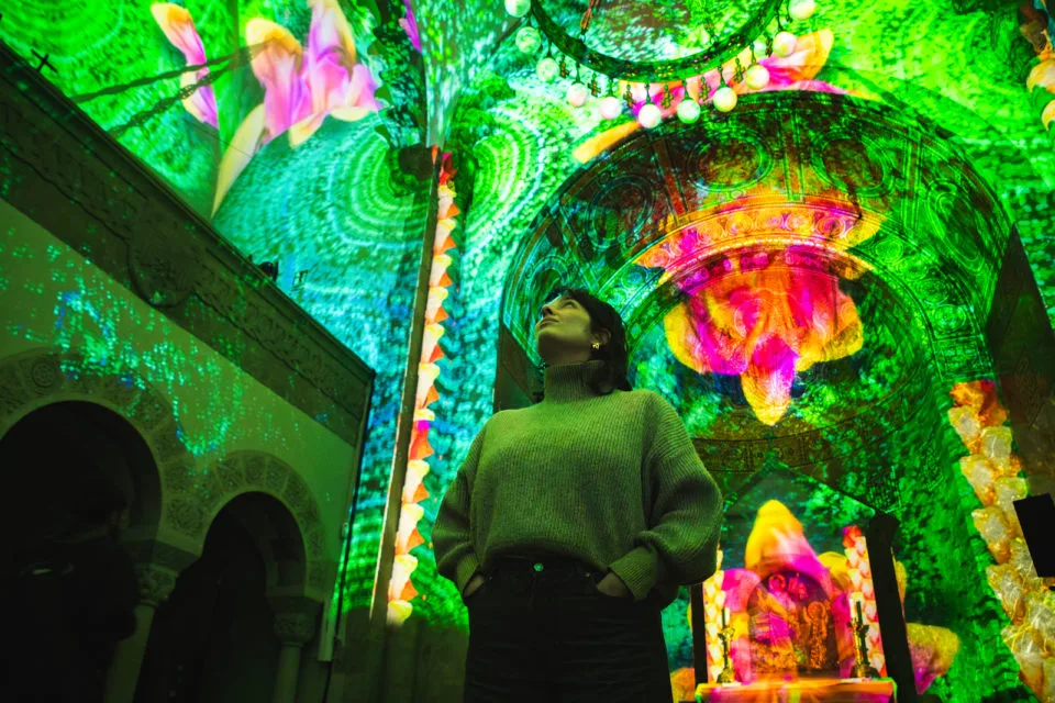 A person admires the green and pink florals projected onto the interior of a building