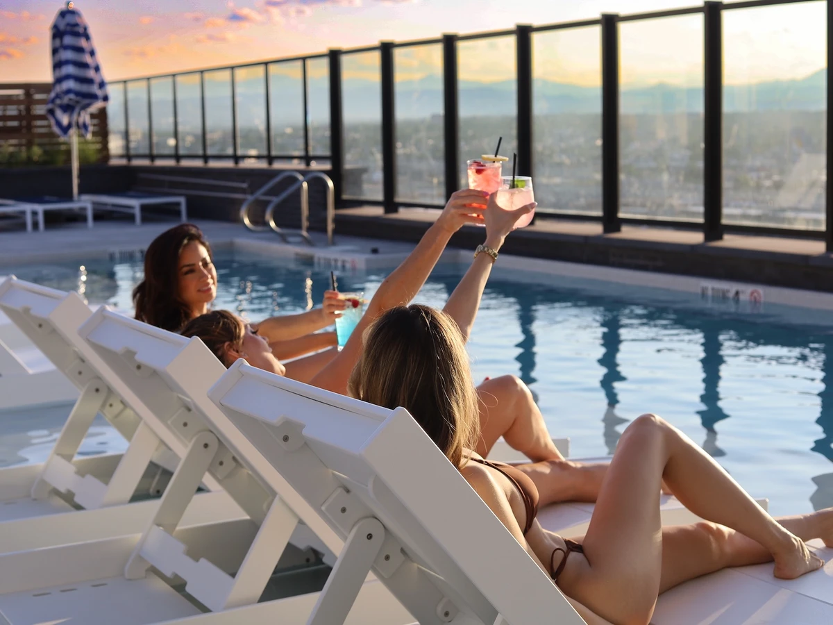 Women in loungers cheers cocktails next to a pool with mountain views