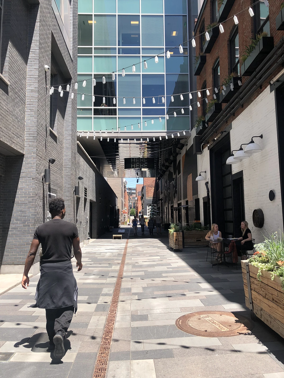 A person walks down the alleyway at Milk Market under string lights made from milk bottles