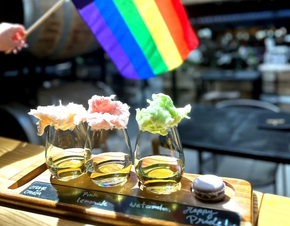 A wine flight with a rainbow Pride flag in the background 