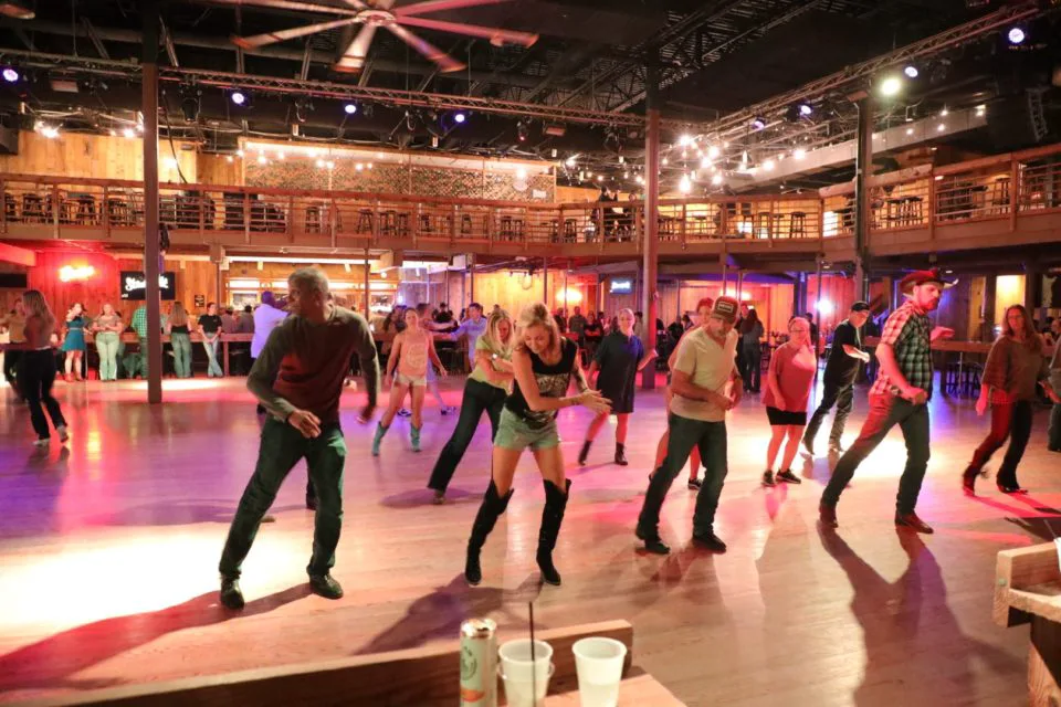 A crowd of people line dances on the dance floor of the Stampede