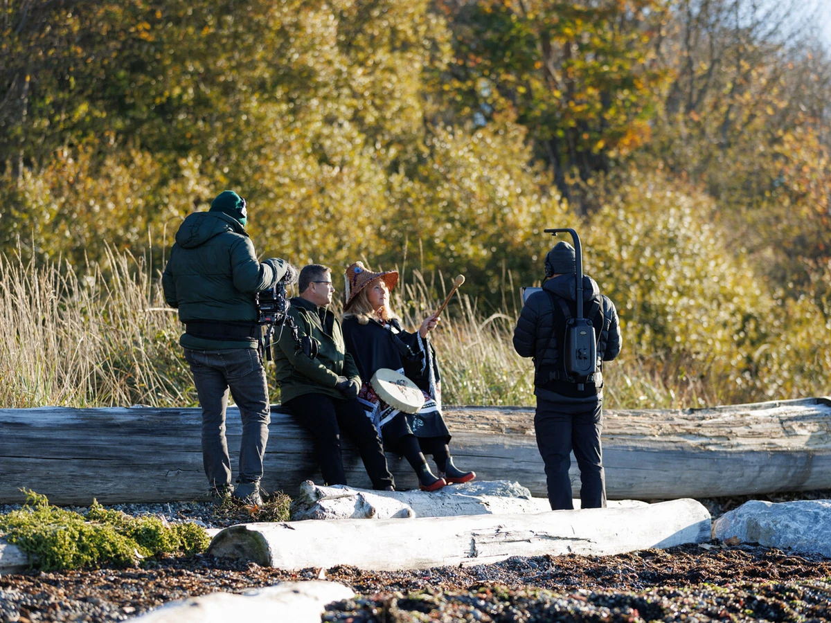 Man and woman sitting on a tree trunk in front of cameras