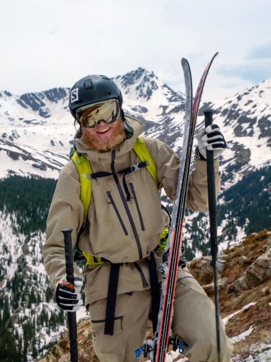 Drew Petersen wearing khaki ski garb in front of mountains