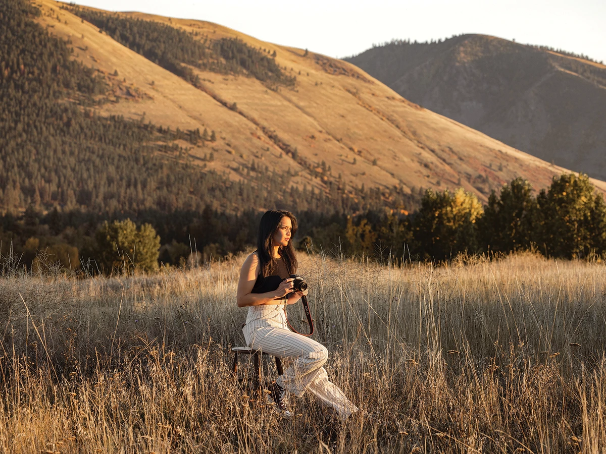 Woman sitting in golden landscape holding camera