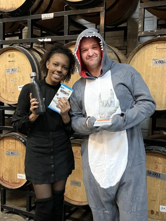 A woman and man smiling, dressed in halloween costumes, holding up prizes.
