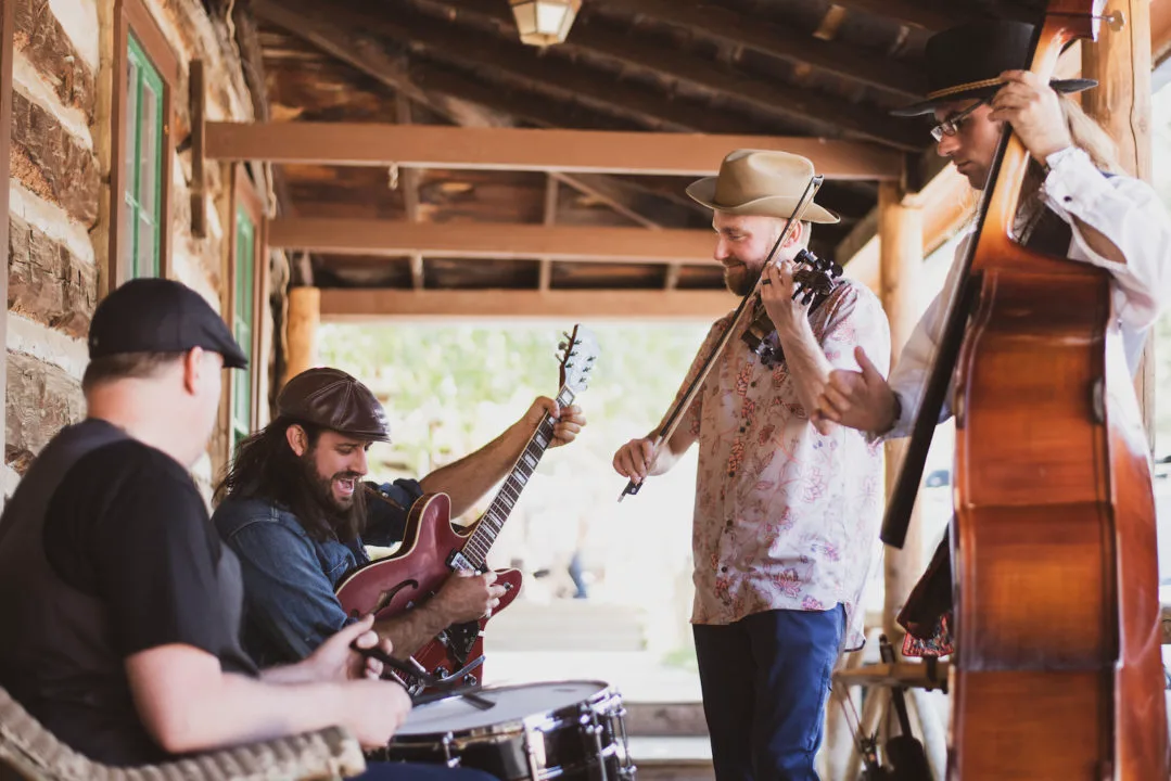 A photo of the band David Lawrence and the Spoonful playing stringed instruments on a porch. Photo by Roxie Photo