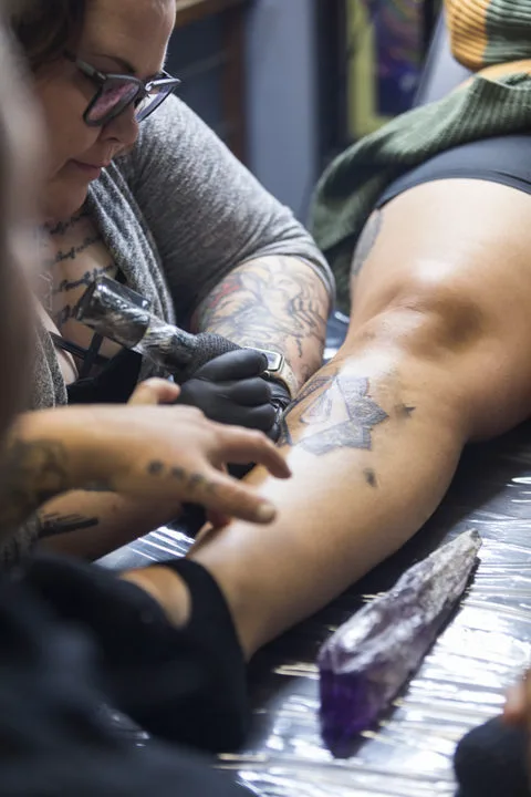 woman tattooing an ornate shape on a client's shin