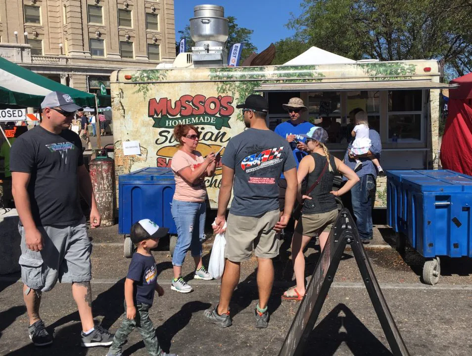 People standing in front of Musso's food truck at a street festival.